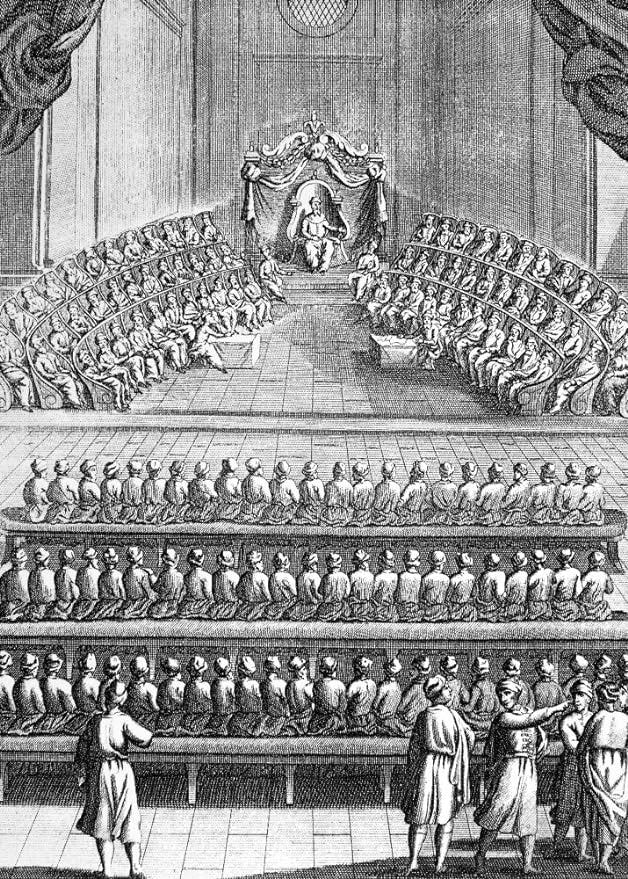A black and white image with a dude at the front and a lot of dudes sitting in semicircircle around him, and then a bunch of benches facing the semicircle, full of dudes